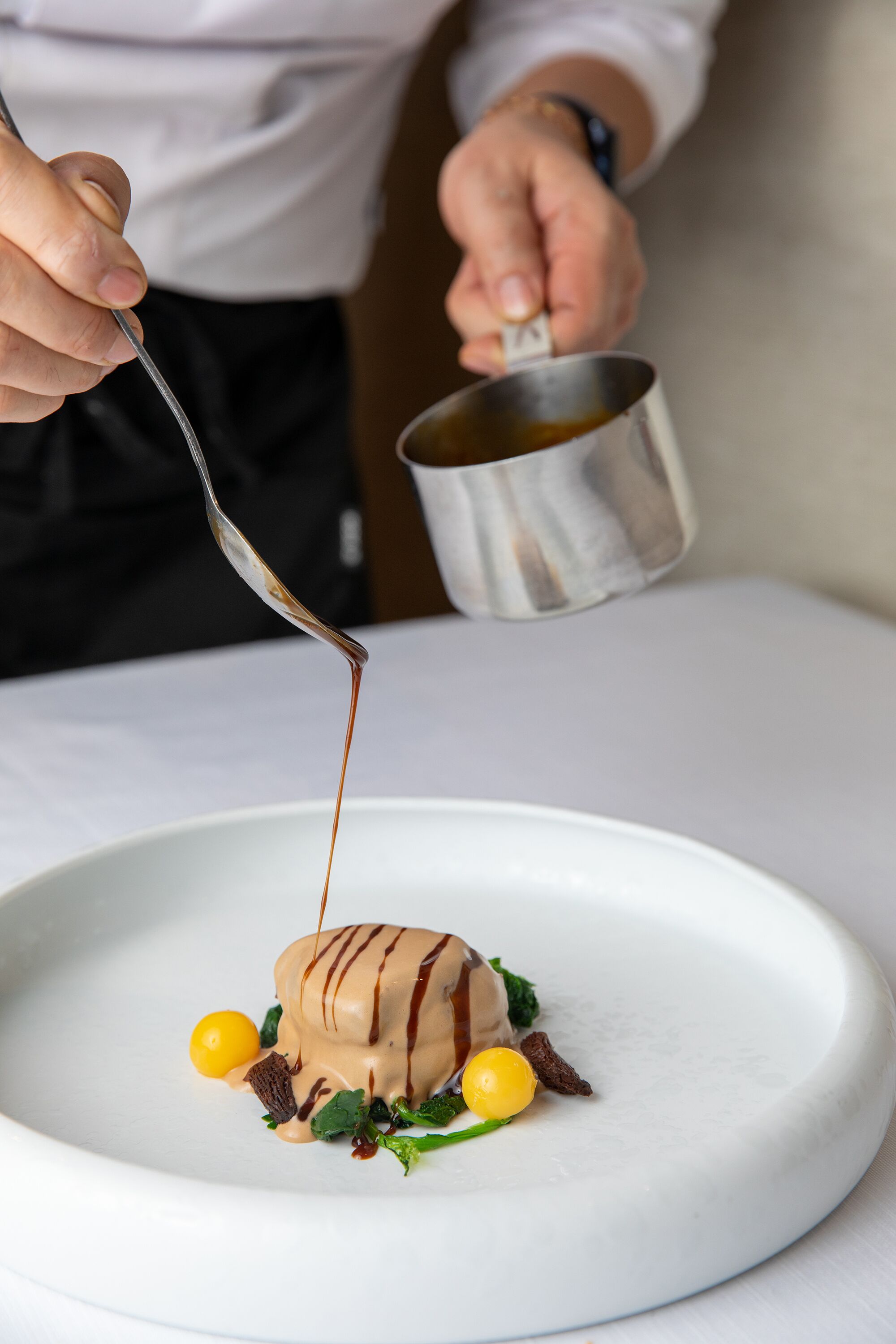 Une personne verse de la sauce sur un dessert présenté dans une assiette blanche.