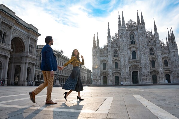 A couple walking in a plaza with a historic cathedral in the background.