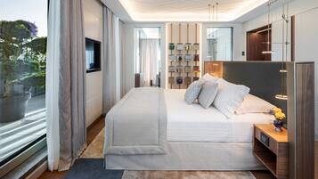 A modern bedroom with a large bed, a bedside table with a lamp, a mirror, and a view of the outdoors.