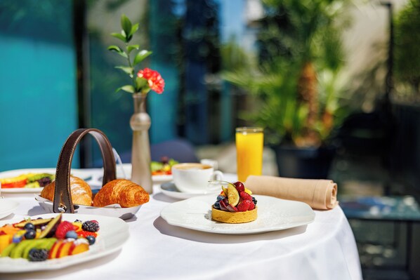 Desayuno con croissants, fruta y una bebida en una mesa al aire libre.