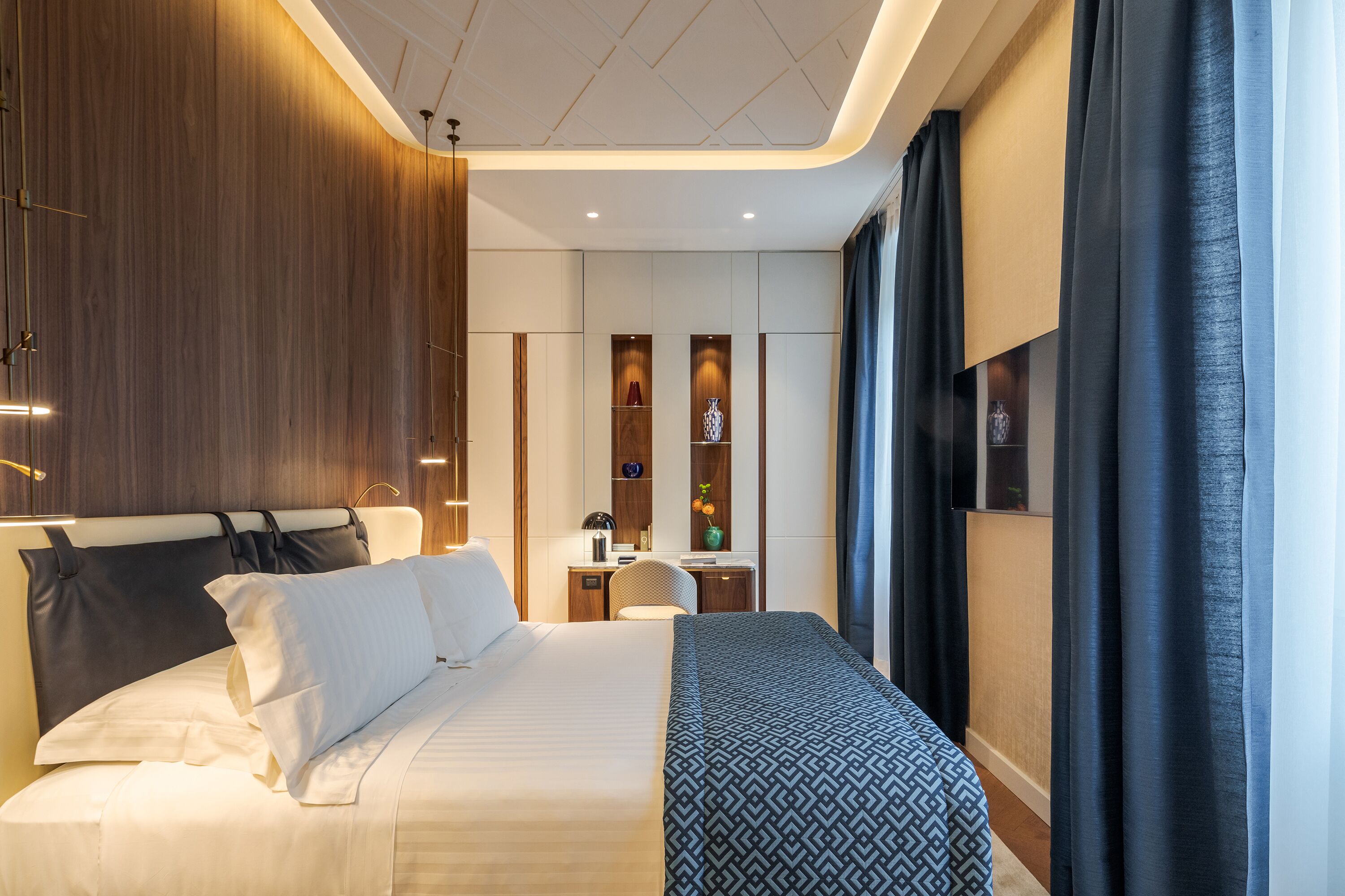 A modern hotel room with a large bed, a desk, and a wardrobe.