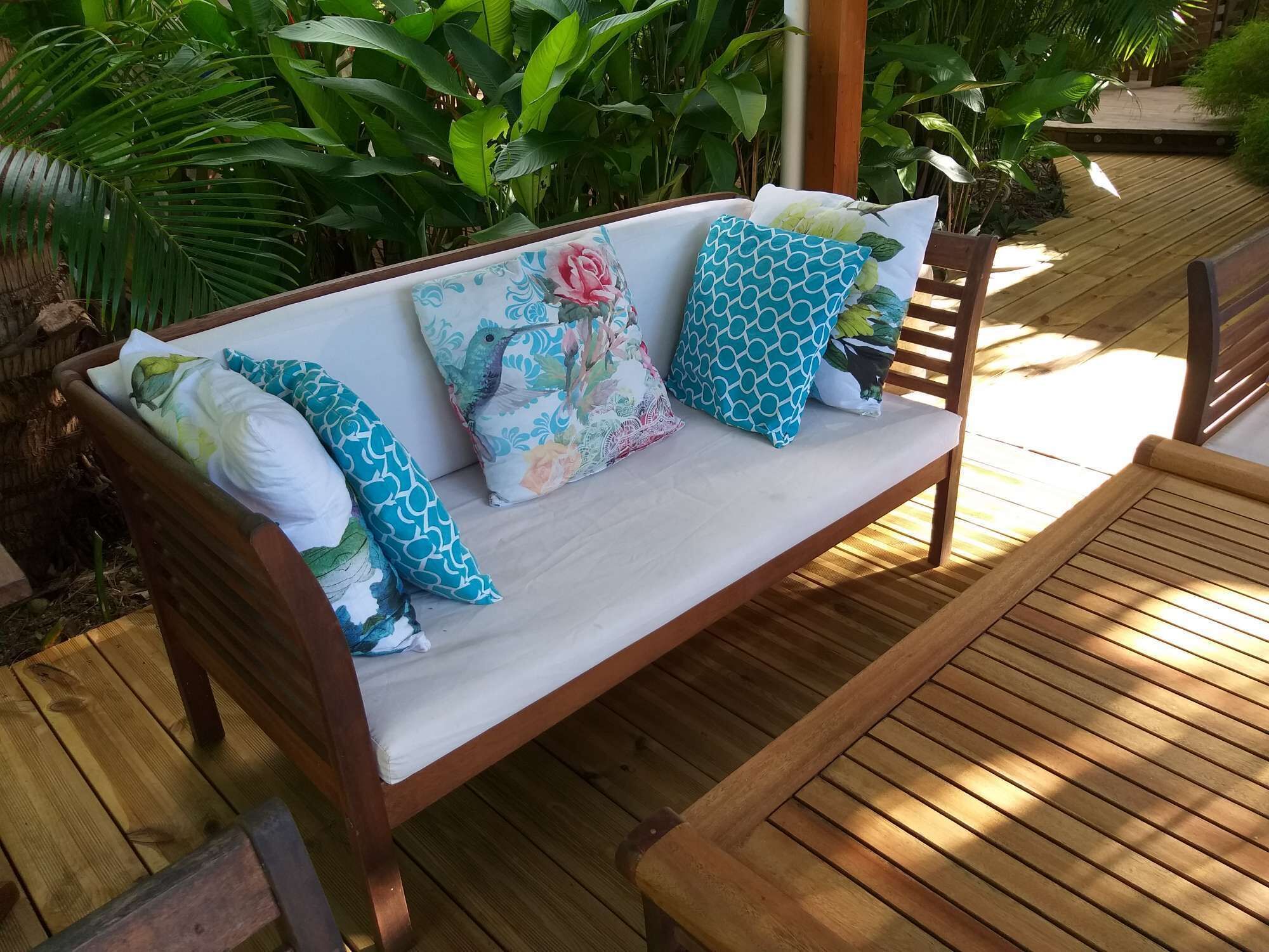 A wooden bench with a cushioned seat and backrest, surrounded by lush green plants.