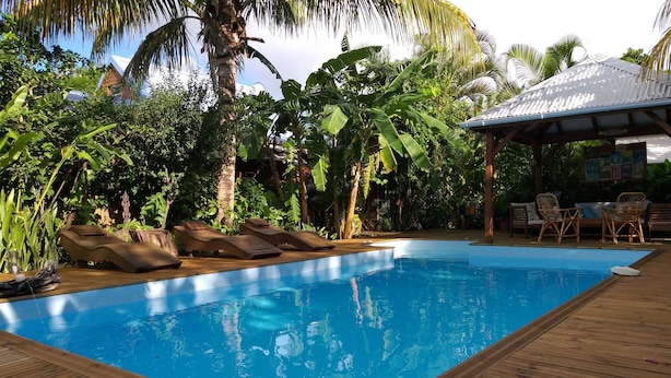 Piscina com deck de madeira e espreguiçadeiras, rodeada por vegetação tropical.