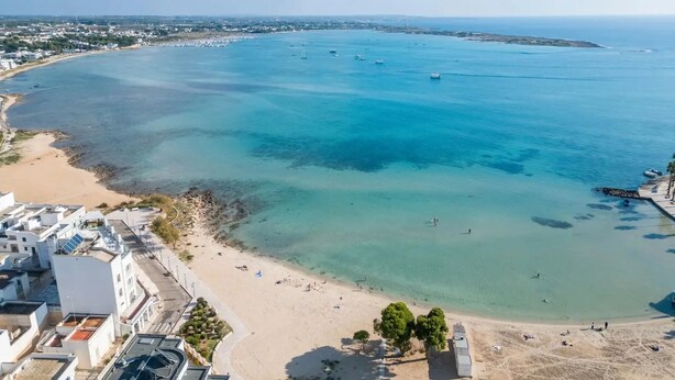 Ein Luftbild einer Küstenregion mit sandigem Strand, klarem blauen Wasser und einigen Booten.