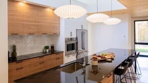 A modern kitchen with a central island, wooden cabinets, stainless steel appliances, and pendant lighting.