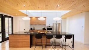 A modern kitchen with a large island, black bar stools, and pendant lighting.