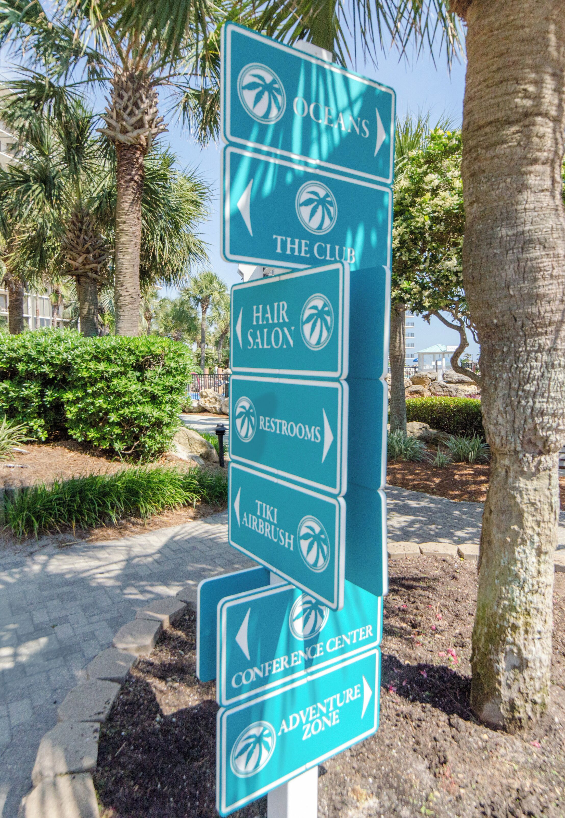 A directional sign with arrows pointing to various amenities such as the club, hair salon, restrooms, tiki airbrush, conference center, and adventure zone.