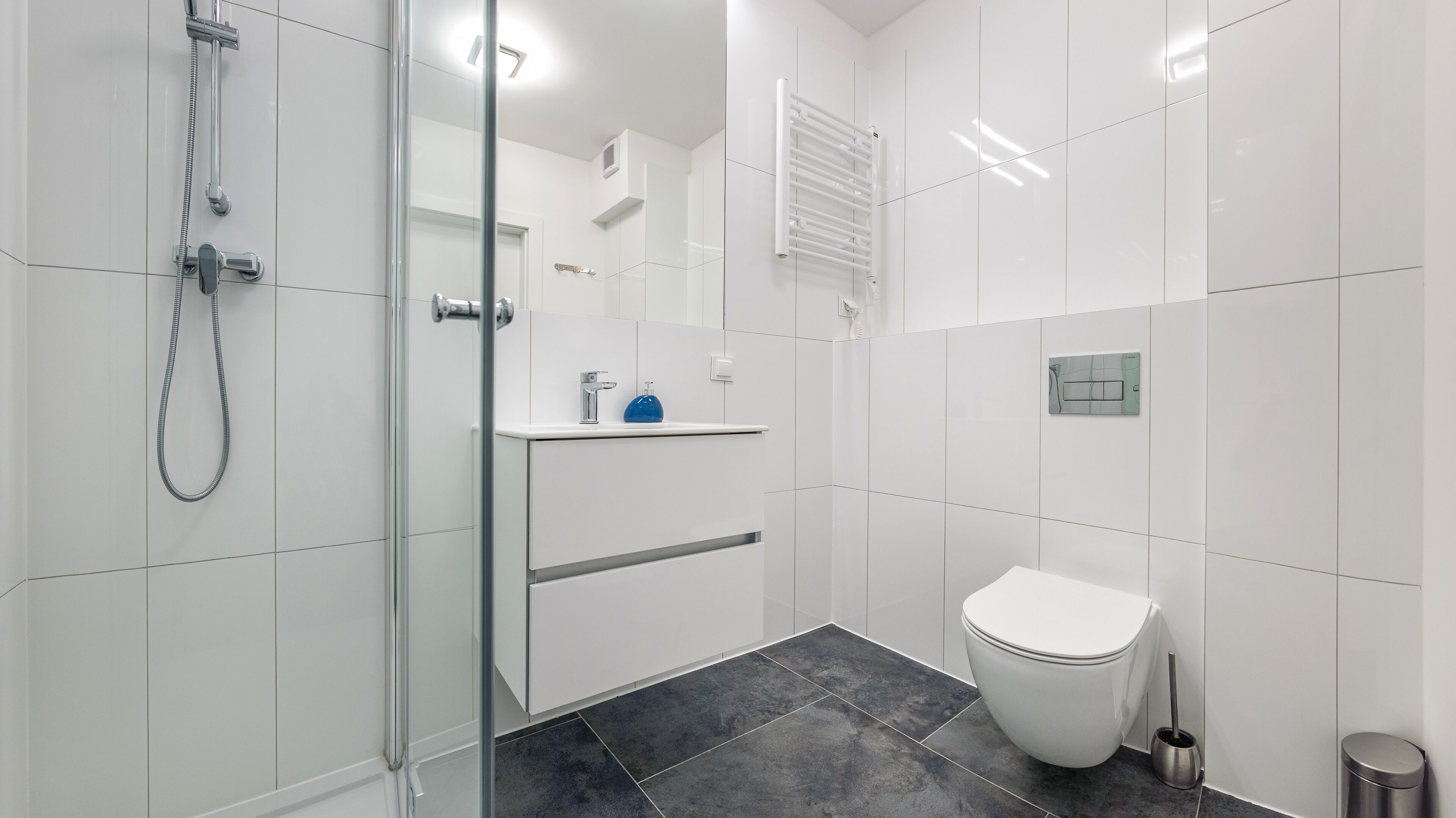 Un baño moderno con cabina de ducha de vidrio, inodoro blanco y lavamanos con dispensador de jabón.