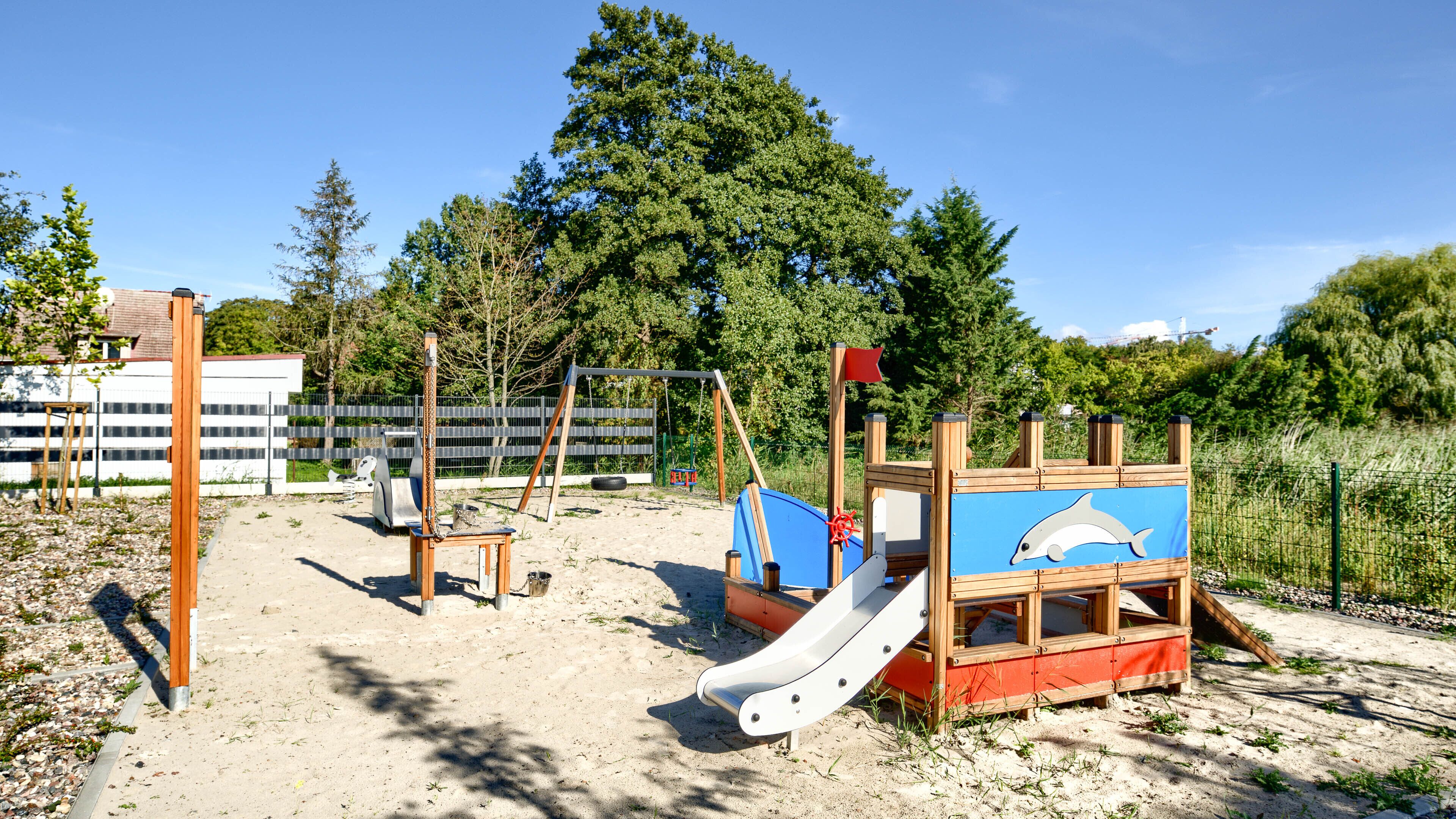 A playground with a slide, climbing structures, and a blue playhouse with a dolphin design.