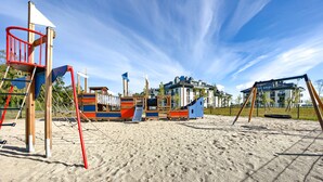 Ein Spielplatz mit verschiedenen Spielgeräten, darunter Rutschen und Schaukeln, auf sandigem Untergrund.