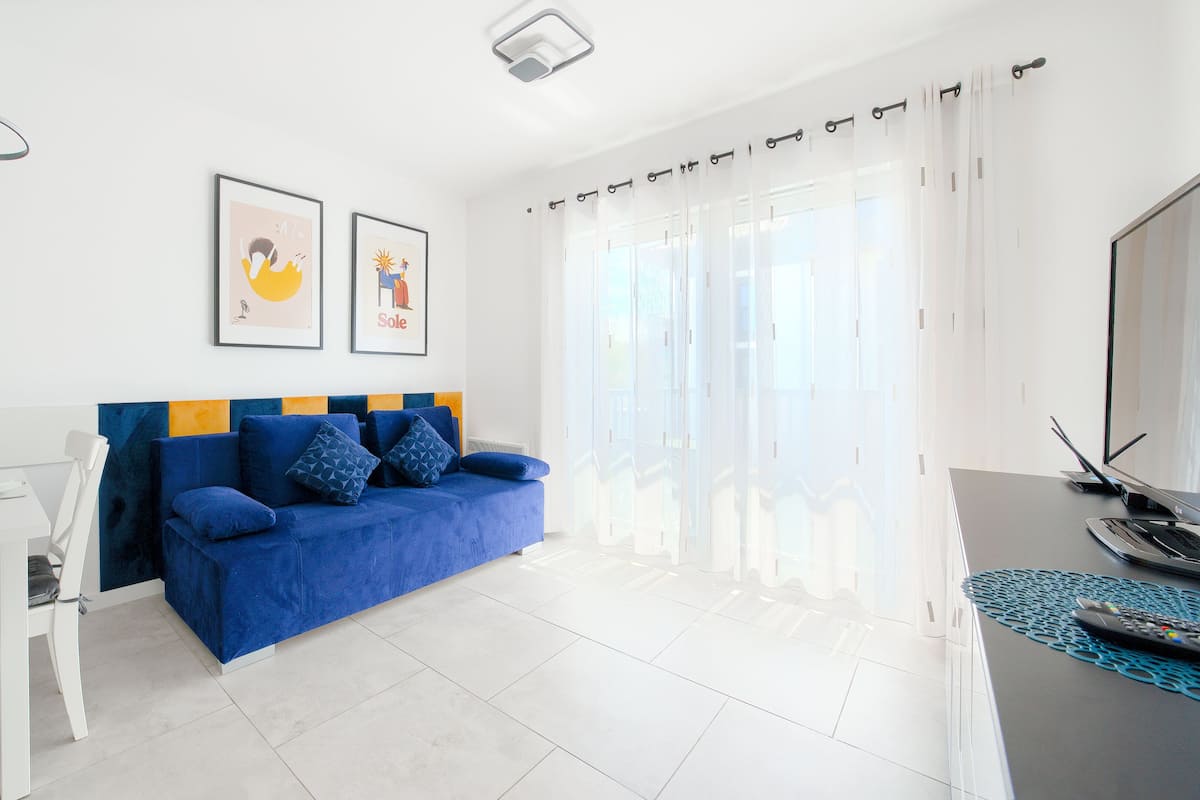 Ein modernes Wohnzimmer mit einem blauen Sofa, weißen Wänden und einem Essbereich mit einem weißen Tisch und Stühlen.