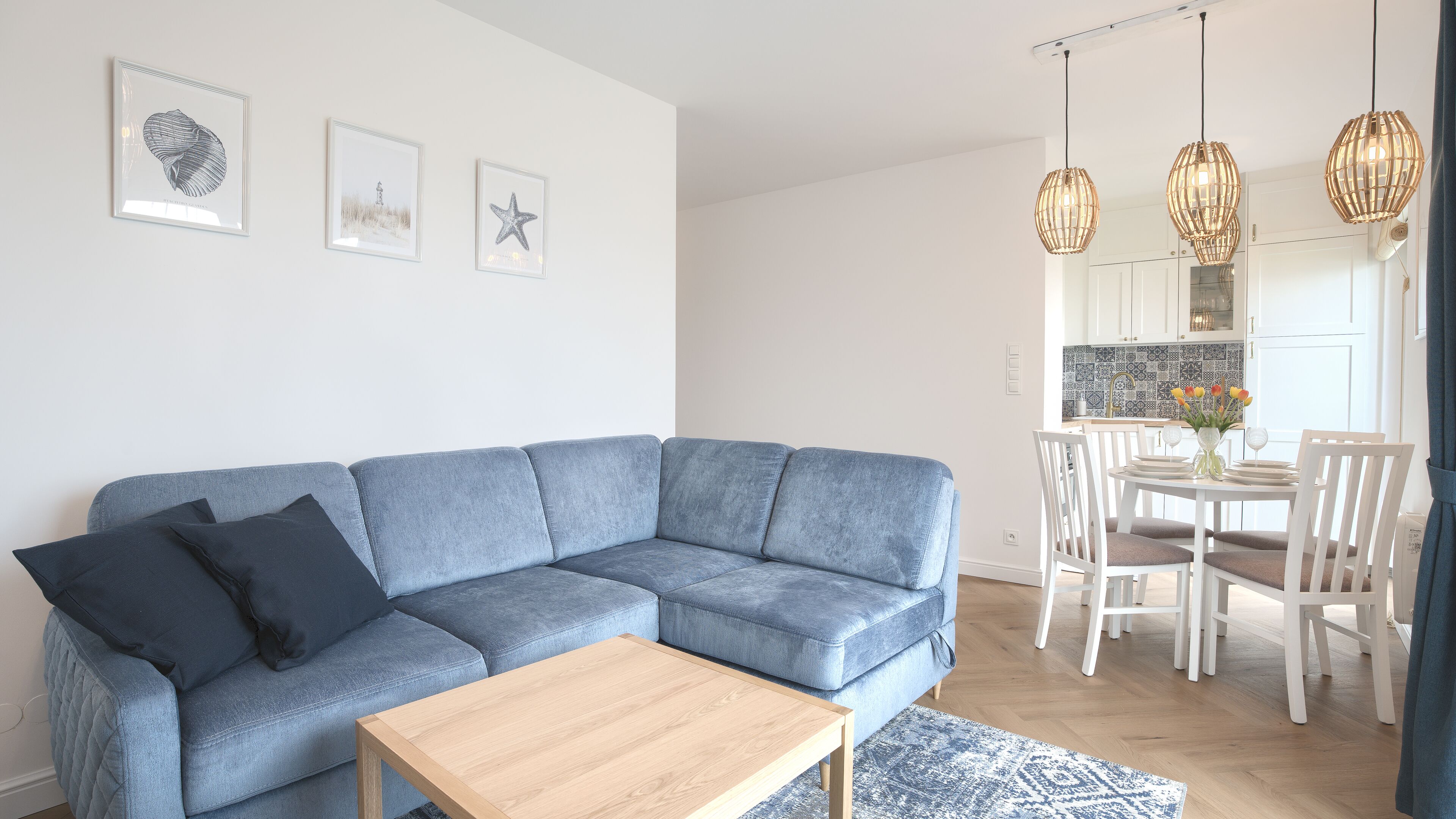 A modern living room with a blue sectional sofa, a wooden coffee table, and a dining area with white chairs and a table.