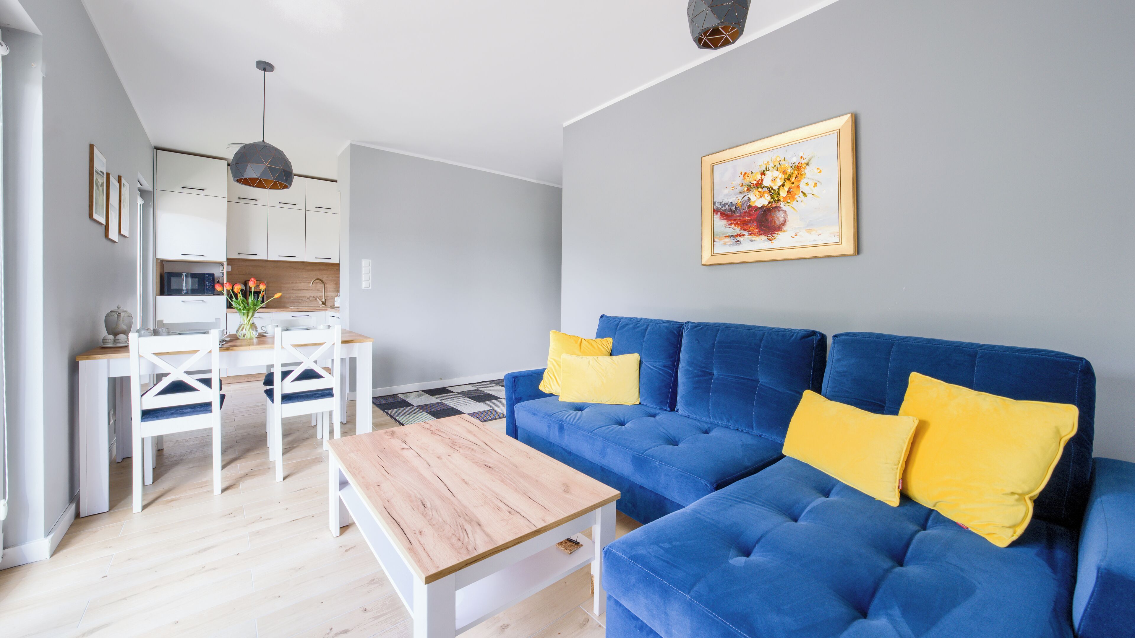 Ett modernt vardagsrum med en blå soffa, ett träbord som används som soffbord och en matplats med ett vitt bord och stolar.