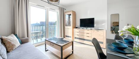 Moderni hotellihuone, jossa on parveke, taulutelevisio, puinen lipasto ja ruokailutila, jossa on sinivärinen astiasto.