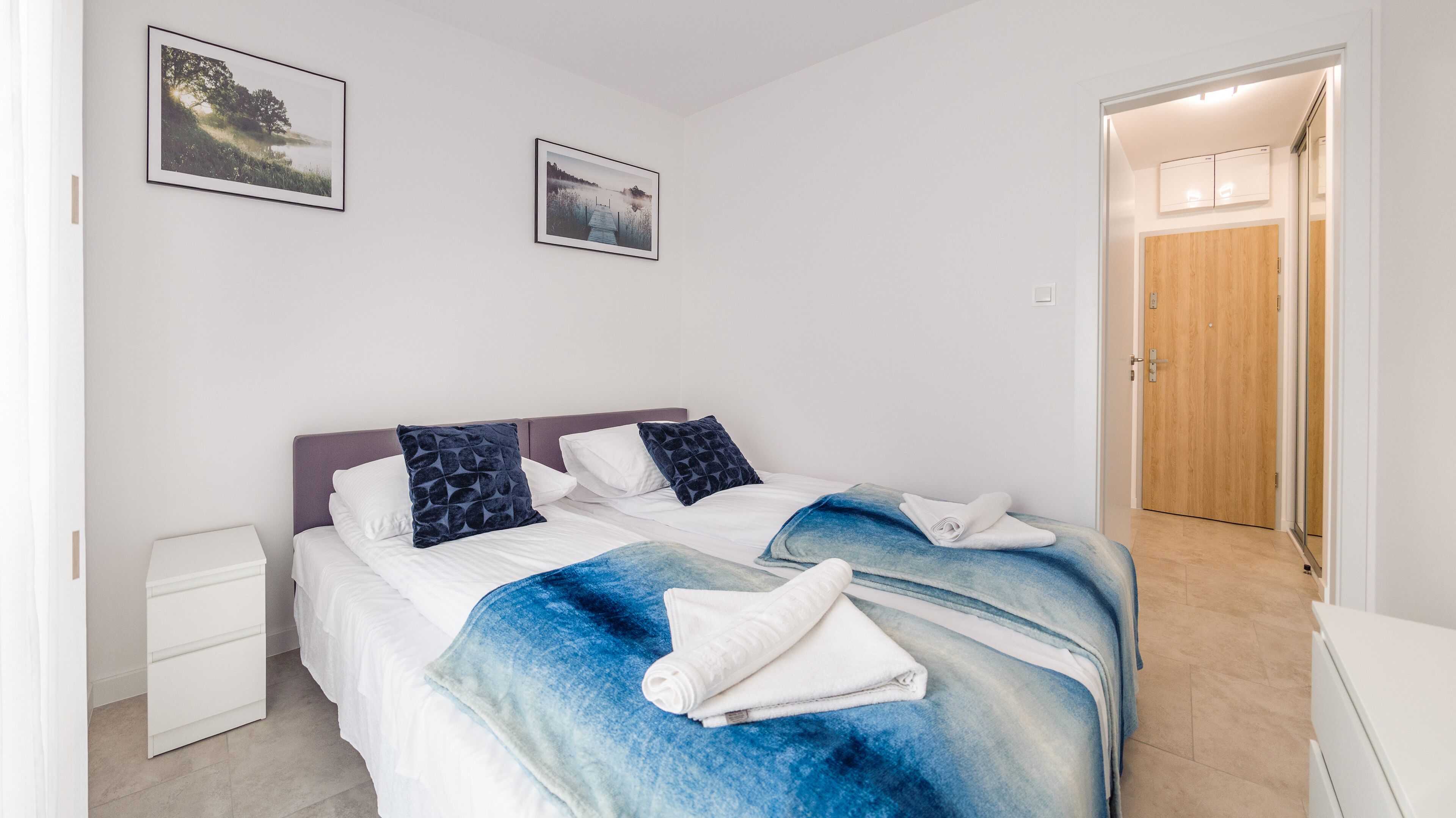 Ein Schlafzimmer mit einem Bett, zwei Kissen, einem Nachttisch und einer Tür zu einem anderen Raum.