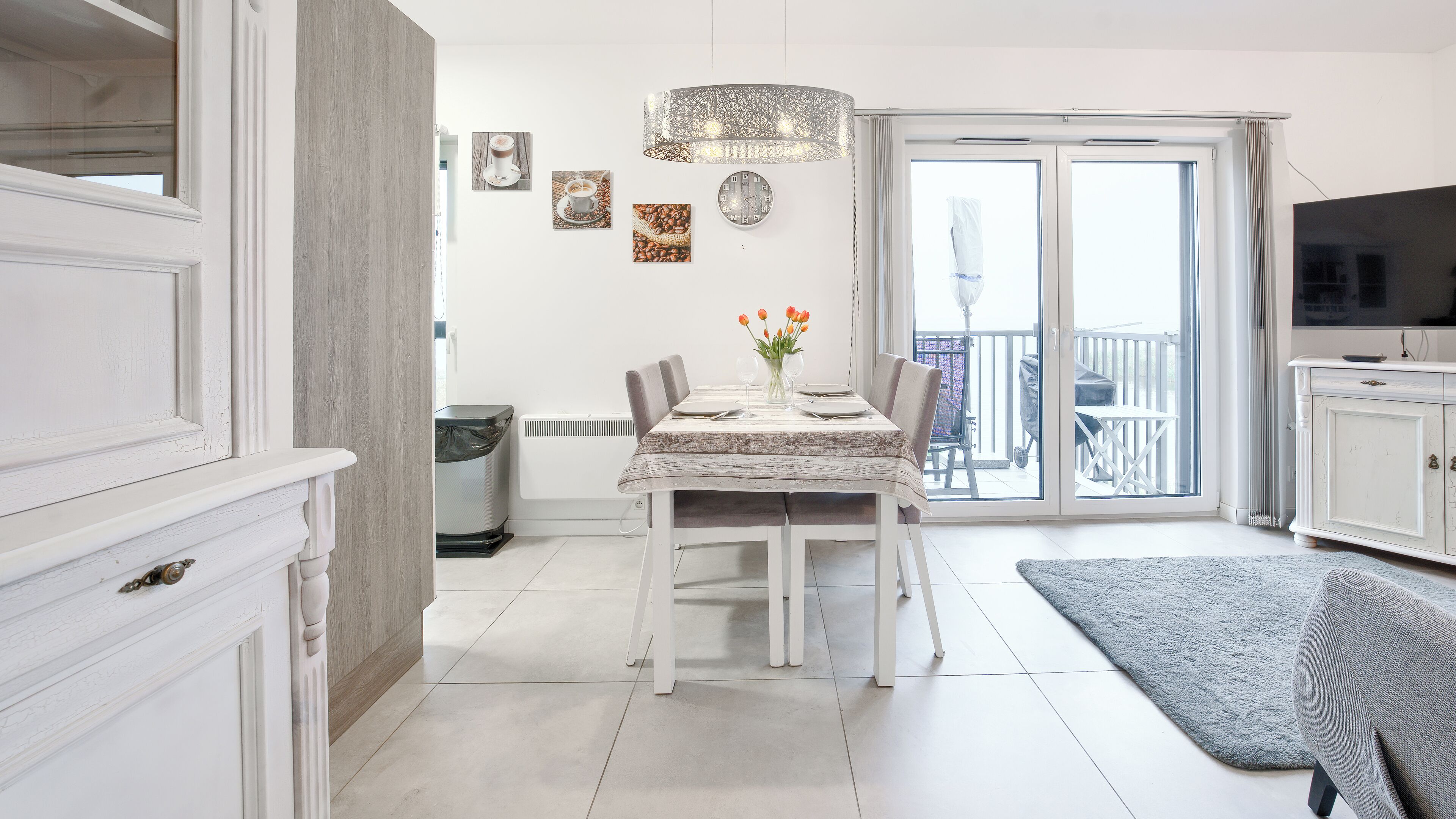 A modern kitchen with white cabinetry, a dining table set for four, and a large window with a view of the outdoors.