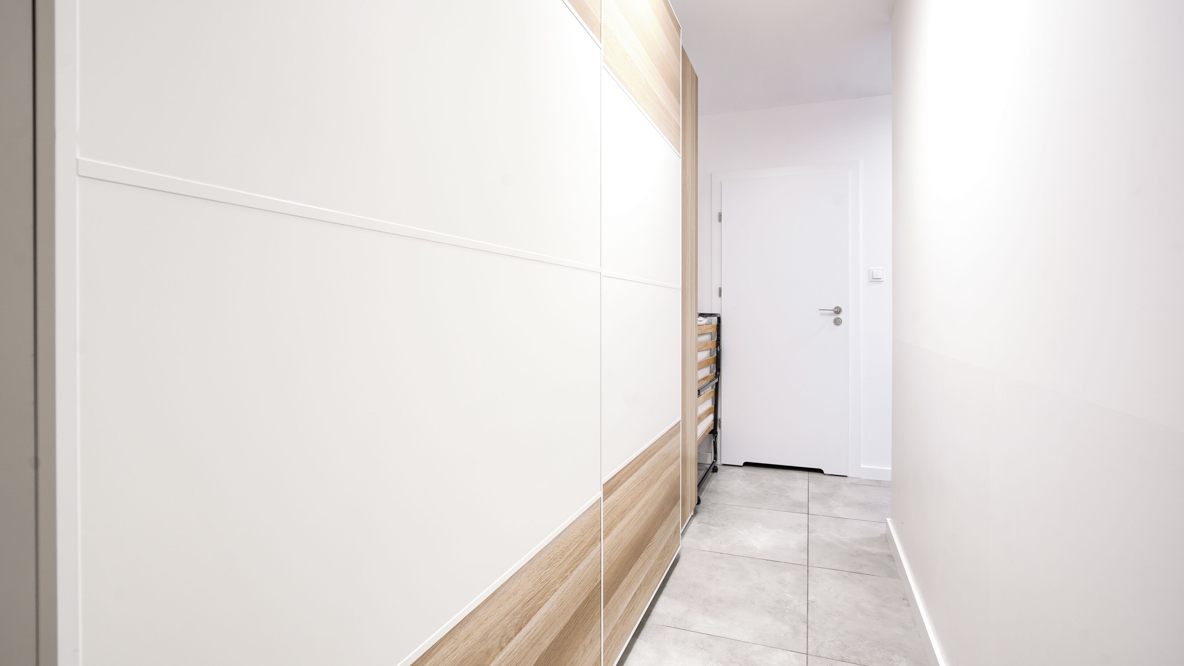 A hallway with white walls and a wooden accent wall, leading to a door.