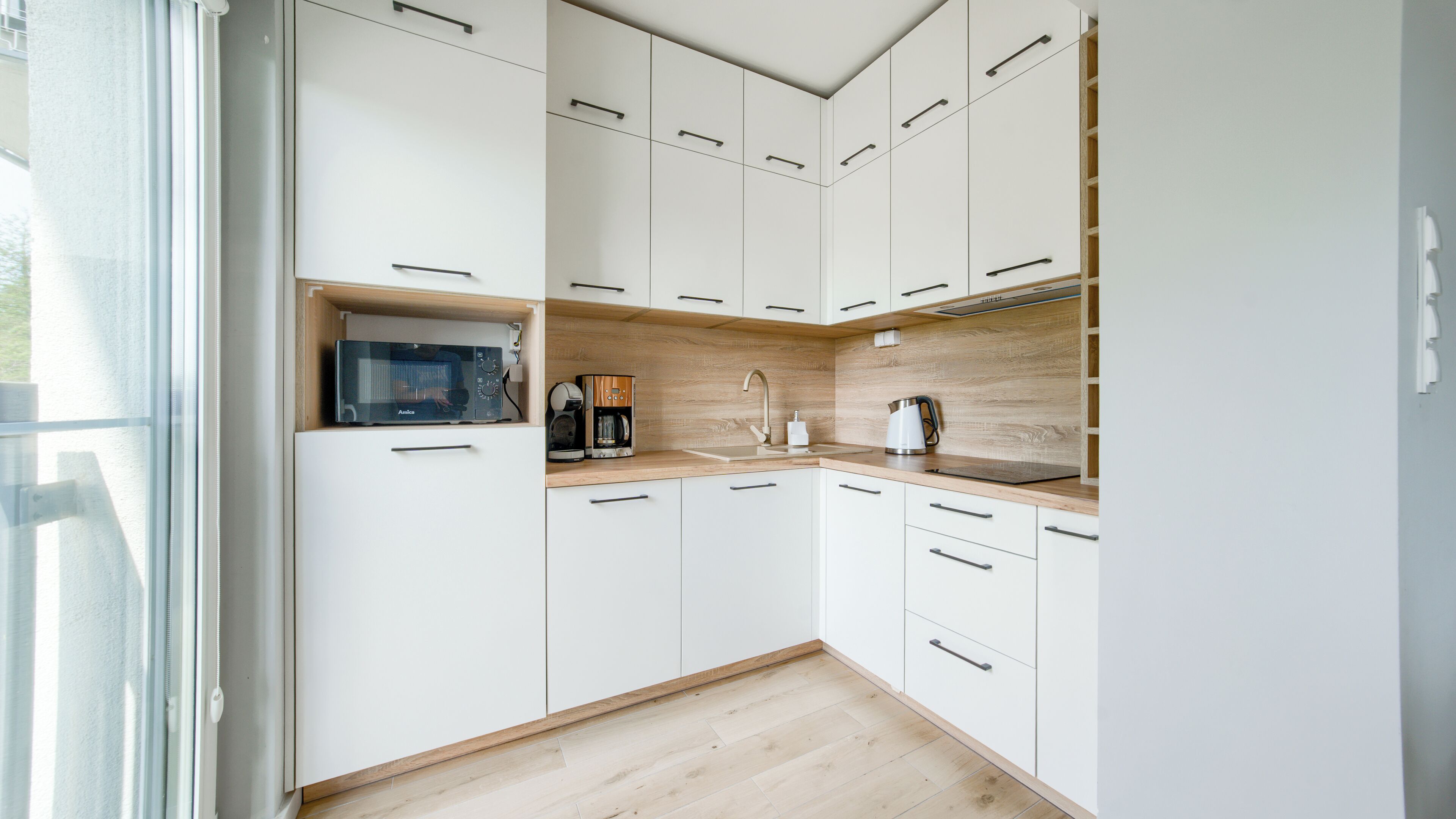 A modern kitchen with white cabinets, a wooden countertop, and a built-in microwave.