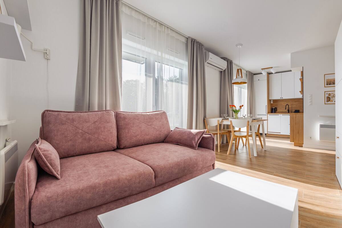 Ein modernes Wohnzimmer mit einem rosa Sofa, einem weißen Couchtisch und einem Essbereich mit einem Holztisch und Stühlen.