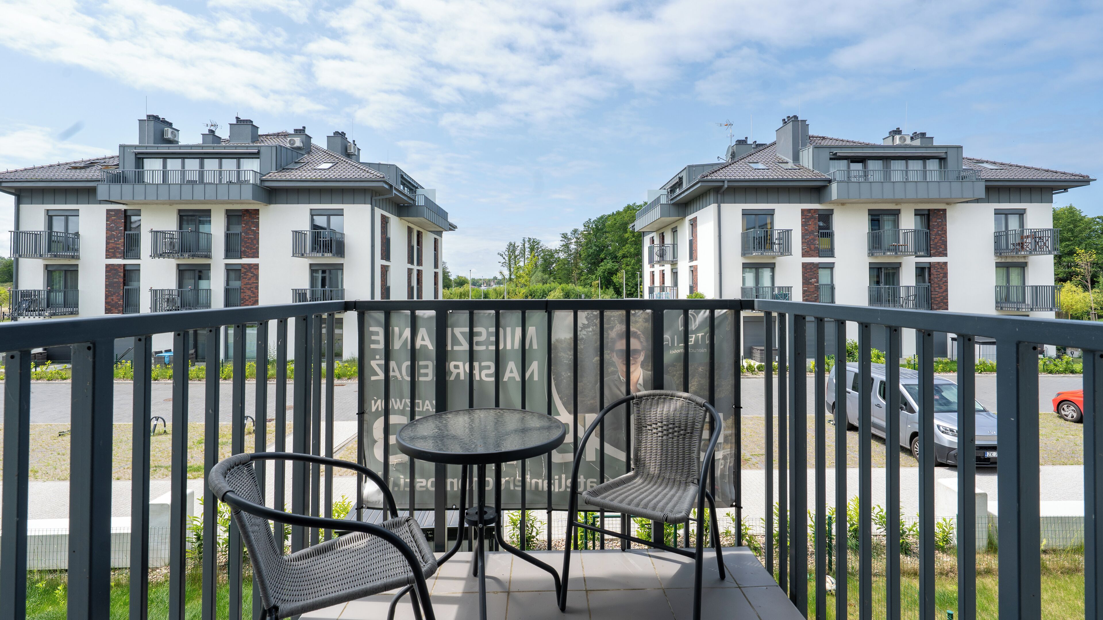 Een balkon met een tafel en stoelen, met uitzicht op een parkeerplaats en woongebouwen.