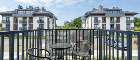 Een balkon met een tafel en stoelen, met uitzicht op een parkeerplaats en woongebouwen.