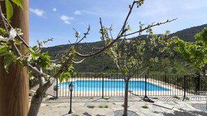 Une piscine entourée d’une terrasse en pierre et d’une clôture en métal, avec en arrière-plan une vue sur un paysage vallonné.