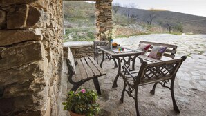 Une terrasse en pierre avec des meubles en bois, notamment un banc et une table, ainsi qu’une plante en pot.