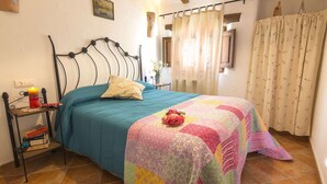Une chambre à coucher avec un lit, une table de chevet sur laquelle se trouve une bougie, et une fenêtre avec des rideaux.