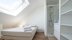 Une chambre avec un puits de lumière, un lit, une petite table de chevet et un dressing avec des étagères.