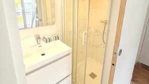 Une salle de bain moderne avec une douche à parois de verre, un meuble-lavabo blanc avec un miroir et un porte-serviettes.