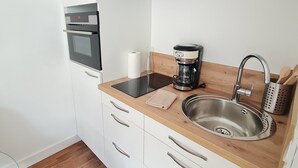 Une cuisine compacte avec des meubles blancs, un évier en acier inoxydable, une machine à café et un four encastré.