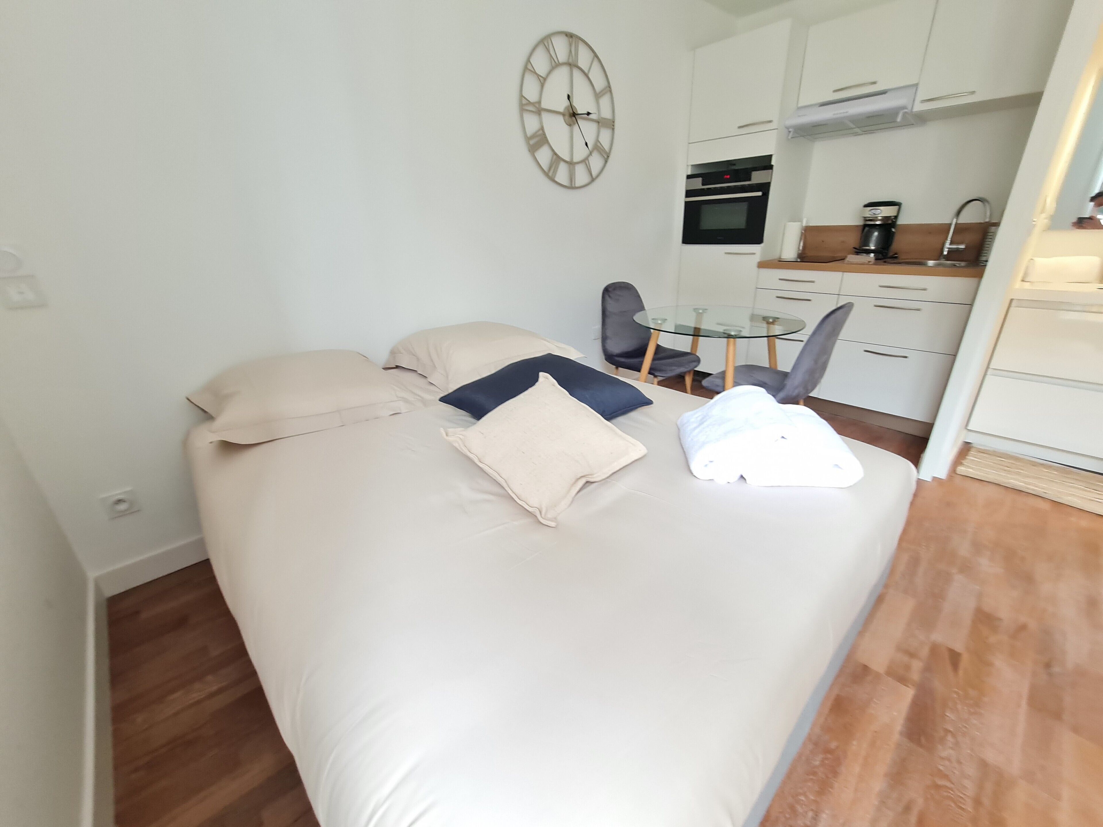Ein kleines Hotelzimmer mit Bett, einem Tisch und einer Küchenzeile.