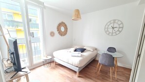 Une chambre moderne avec un lit, un bureau, une chaise, une télévision et une grande fenêtre.