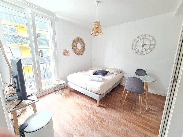 Une chambre moderne avec un lit, un bureau, une chaise, une télévision et une grande fenêtre.