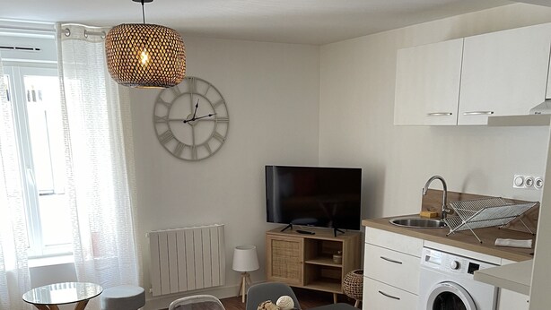 Une cuisine moderne équipée d’un lave-linge, d’une table à manger avec des chaises, d’un téléviseur et d’une grande horloge murale.