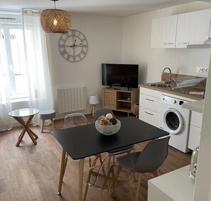 Eine moderne Küche mit Waschmaschine, einem Esstisch mit Stühlen, einem Fernseher und einer großen Wanduhr.