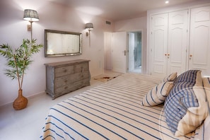 A bedroom with a bed, dresser, mirror, lamp, and a door leading to another room.