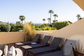 Une terrasse sur le toit, dotée de chaises longues et d’une table, qui offre une vue sur un espace paysager agrémenté de palmiers et sur le panorama de la ville.