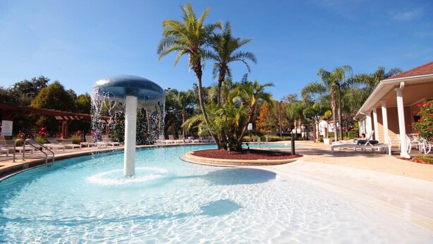 A swimming pool with a water fountain, palm trees, and lounge chairs. - Near Disney: Townhouse w/ Resort Pool & Hot Tub (Kissimmee)