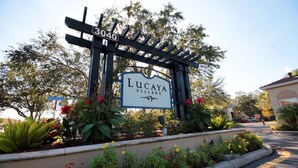 A gated entrance with a sign for Lucaya Village, surrounded by lush greenery and flowering plants. - Near Disney: Townhouse w/ Resort Pool & Hot Tub (Kissimmee)