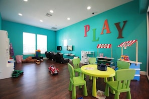 Una sala de jocs infantil amb parets verd blavós, una zona de jocs i una taula amb cadires.