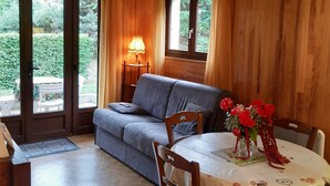 Une pièce chaleureuse avec un canapé gris, une table en bois ornée d’un vase de fleurs rouges et une lampe posée sur une table d’appoint.