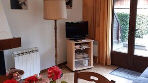 Une pièce confortable avec un téléviseur posé sur un meuble en bois, un radiateur, une porte en bois et une fenêtre avec des rideaux.