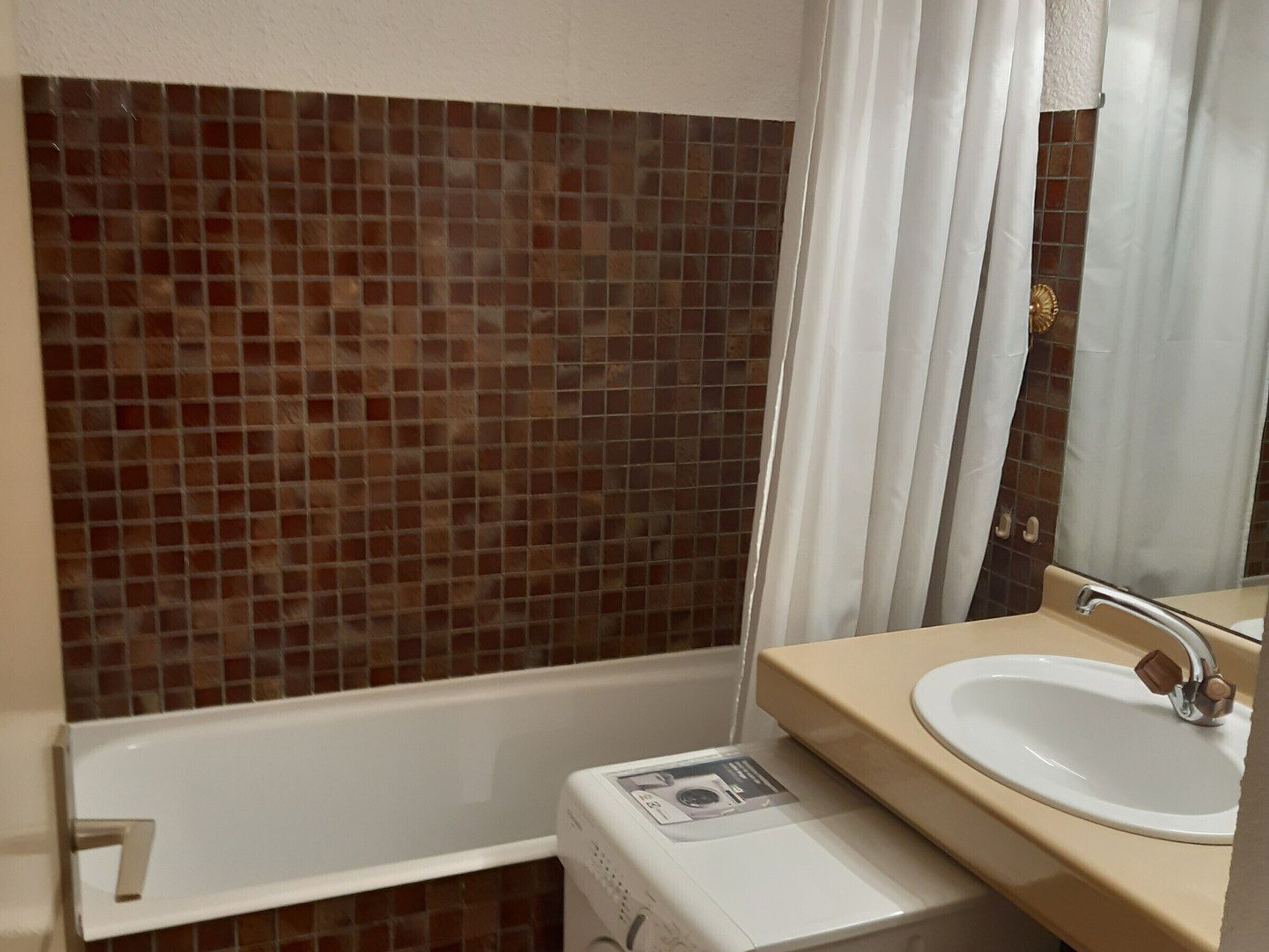 Een badkamer met betegelde wand, een bad, een wastafel en een kleine wasmachine.