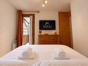 A hotel room with a bed, a wooden dresser, a television, and a view of a building outside.