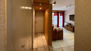 Ein Korridor, der in einen Wohnbereich führt, mit einer hölzernen Bank, einem Fernseher und einem Fliesenboden.