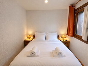 A hotel room with a large bed, two bedside lamps, a window with curtains, and two rolled towels on the bed. - Spacious apartment in Méribel center, close to slopes, for 4, balcony (Méribel)