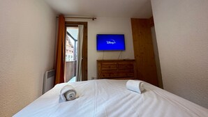 Ein Hotelzimmer mit einem Bett, einem Fernseher mit dem Disney+-Logo, einer Holzkommode und einer Tür zu einem Außenbereich.