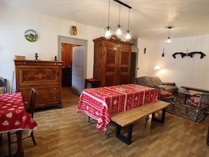 Un coin repas avec un banc en bois, une table recouverte d’une nappe rouge, un buffet en bois et un lustre.