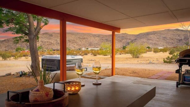 A modern outdoor seating area with a view of a desert landscape and mountains. - 4BR w/ Hot Tub, Space X & Tesla Charger! (Joshua Tree)